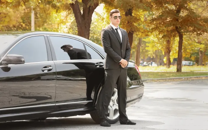 Uniformed chauffeur standing beside a black luxury car in Oslo